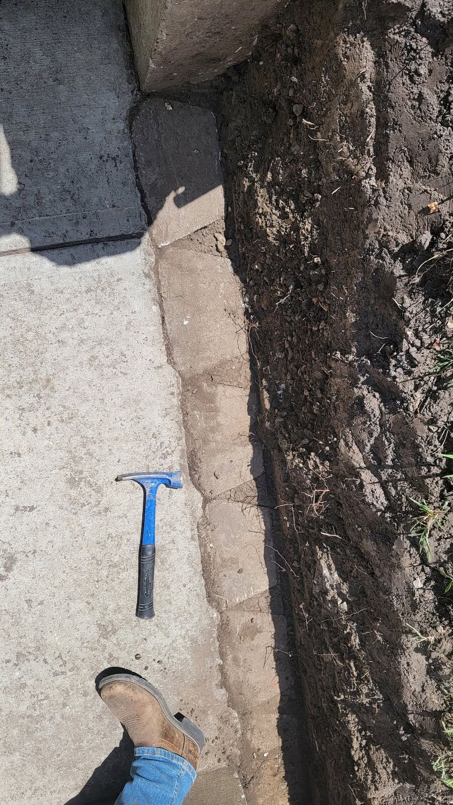 Trench dug along the concrete walk with a hammer for scale